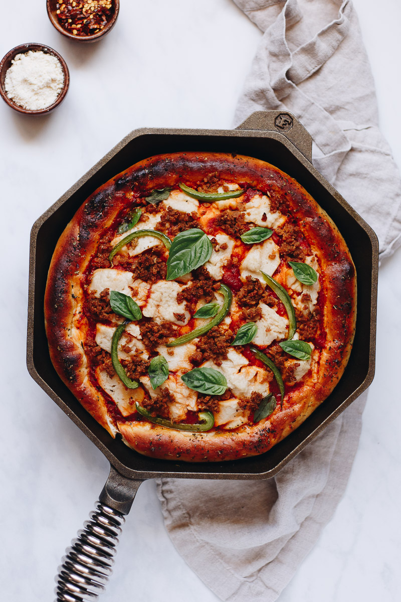 Vegan Deep Dish Pizza by Pasta-based. Thick crust pizza in a hot octagonal-shaped cast iron pan straight out of the oven. Thick golden brown crust, baked in a cast iron skillet with melty vegan mozzarella cheese and homemade plant-based sausage crumbles.