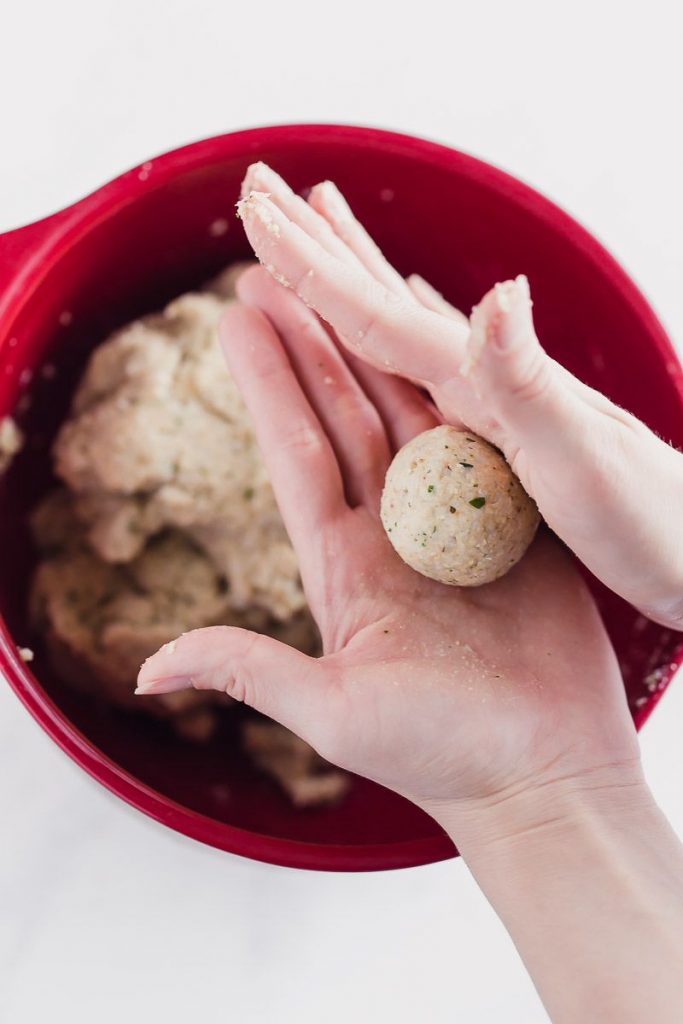 Rolling the uncooked meatball in hands into a ball over a red bowl.