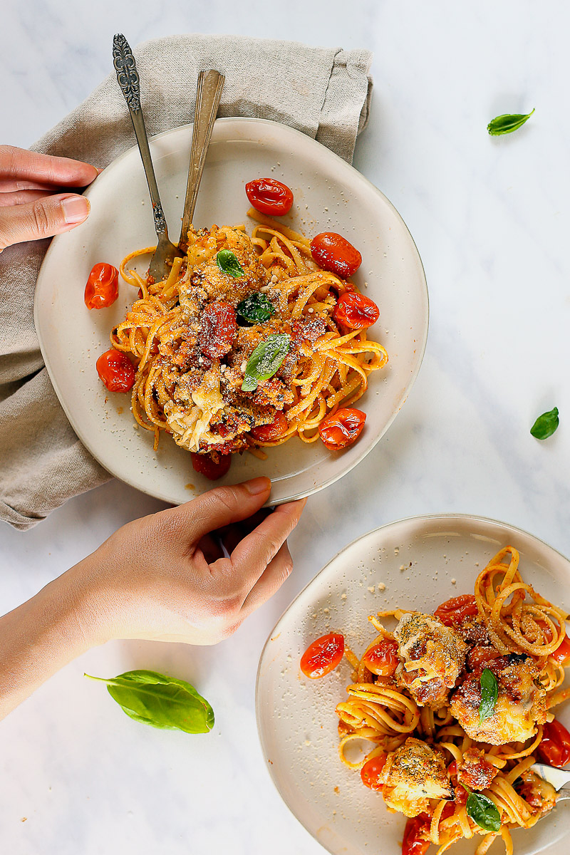 Vegan Cauliflower Parmesan by Pasta-based. Cauliflower parmesan scooped on top of a plate of linguine with two hands coming in to grab the plate.