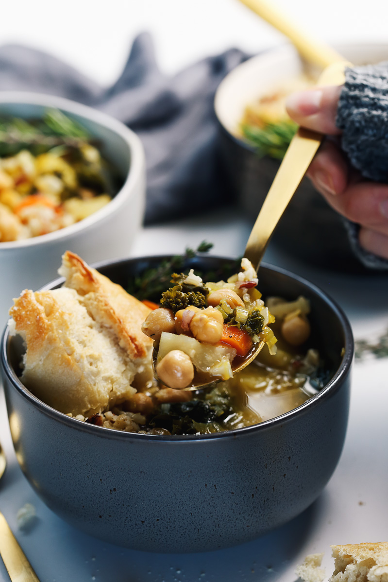 Chickpea Soup by Pasta-based. Hearty, warm, vegetable-filled, chunky, fortifying soup with carrots, celery, leeks, potatoes, garlic, kale, and chickpeas. A piece of crusty bread in the bowl is perfect for dipping.