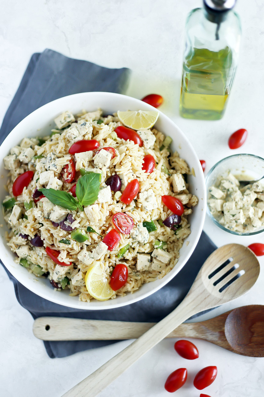 Vegan Orzo Pasta Salad by Pasta-based. A large white bowl piled high with orzo salad. Sprinkled with Homemade Tofu Feta, fresh grape tomatoes, and Dijon Mustard Vinaigrette.