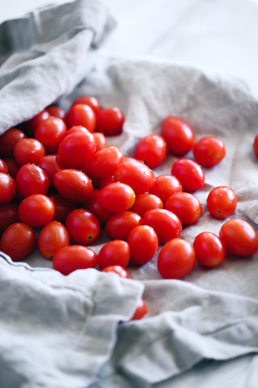 beautiful, bright red, plump grape tomatoes with droplets of water spilling out of a soft linen towel.