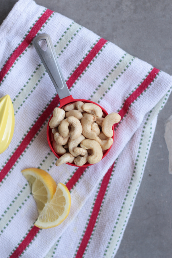 Easy White Wine Vegan Alfredo Sauce.  Red and white striped dish towel, with a red measuring cup filled with raw whole cashews.  Lemon wedges scattered around.