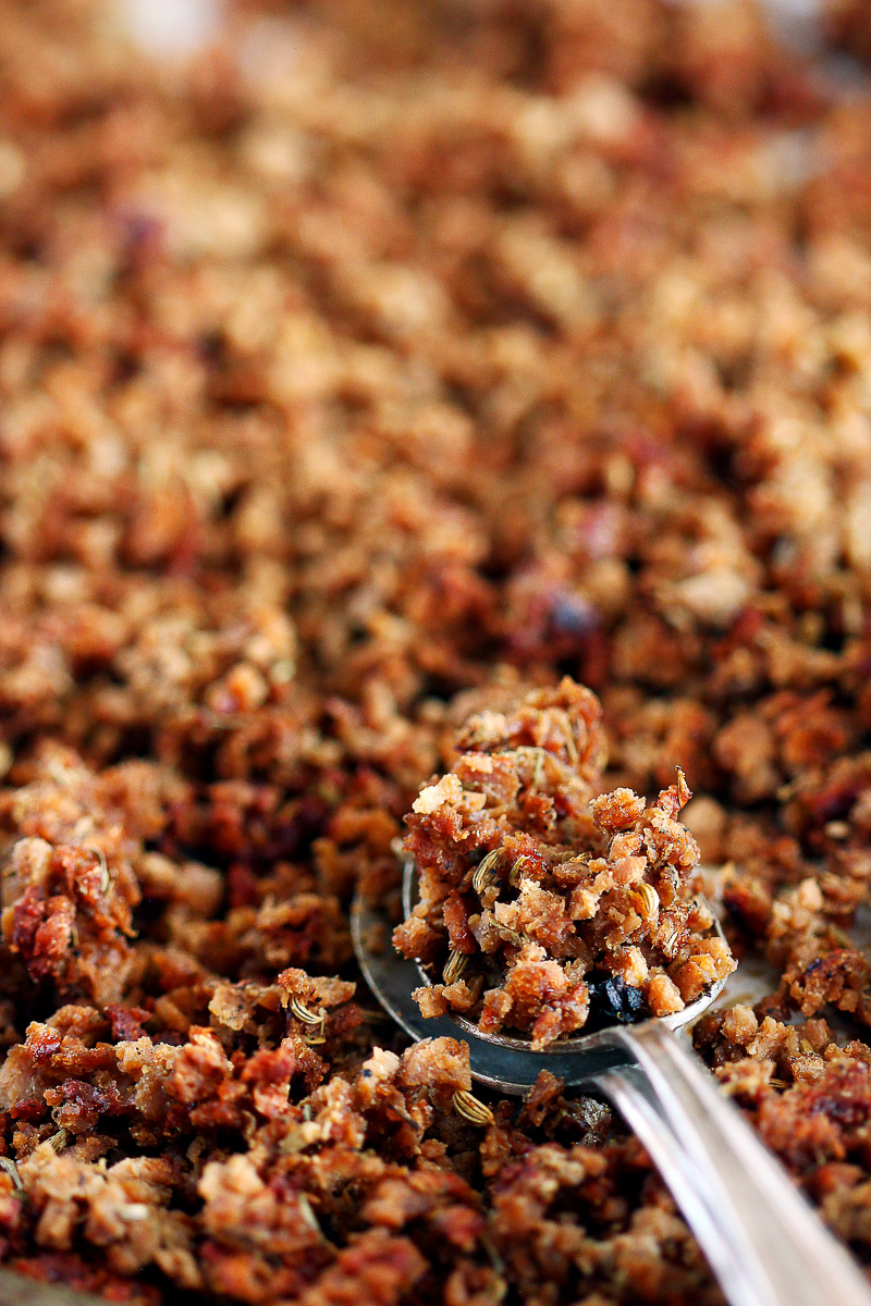 Vegan Italian Sausage Crumbles by Pasta-based. The camera zooms into the vegan Italian sausage crumbles which look mouthwatering straight out of the oven. They are darker in color, crispy in texture, and loaded with aromatic spices like dried fennel seeds which you can see in the photo. Two spoons overlapping lay on the pan with a pile of vegan Italian sausage crumbles in the top spoon.