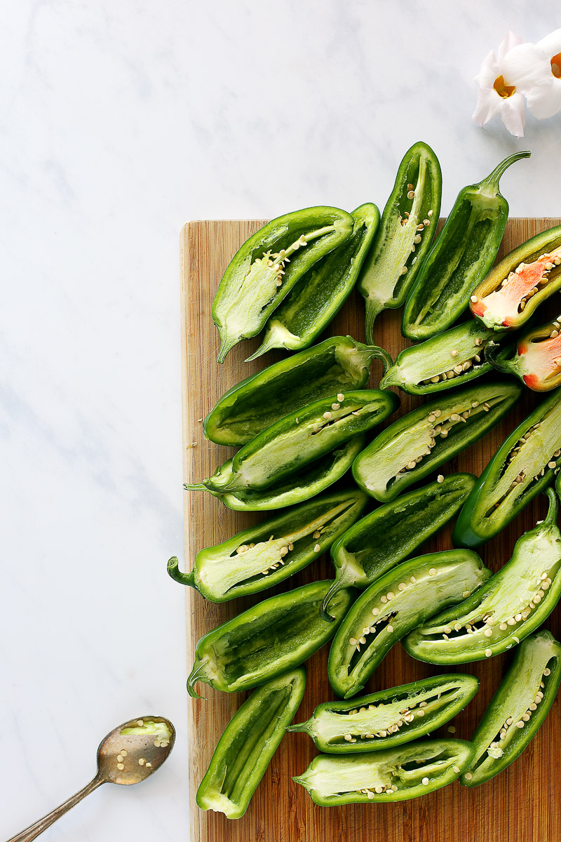 Vegan Jalapeño Poppers by Pasta-based. Bright green, fresh jalapeños sliced in half on a cutting board.