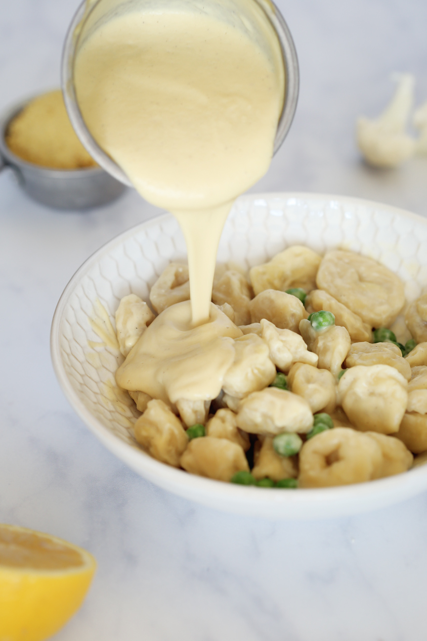 Alfredo sauce being poured on vegan tortellini.