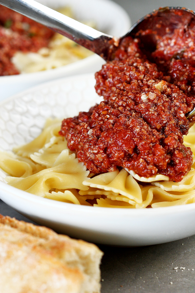 A big scoop of cauliflower walnut bolognese poured on top of a bowl of pasta.