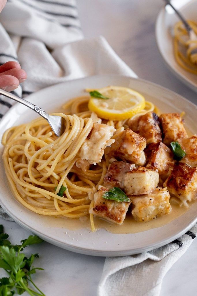 Vegan chicken francese on a fork with spaghetti twirled around it.  Plate with spaghetti and tofu francese on it below.