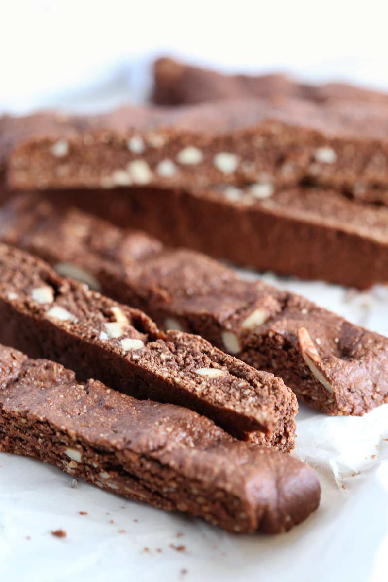 Close shot of chocolate almond lavender biscotti. Dark brown, chocolate-ly crispy cookies with bits of blanched almonds throughout, perfect for dipping in coffee, on a white table.