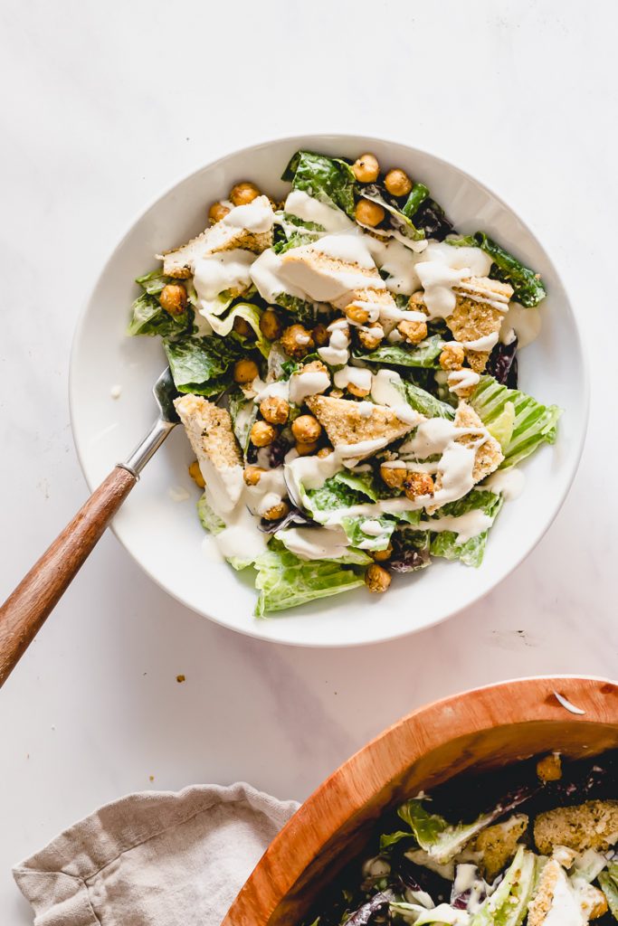 White bowl with lettuce, crispy tofu, crispy chickpeas and vegan caesar dressing drizzled on top.