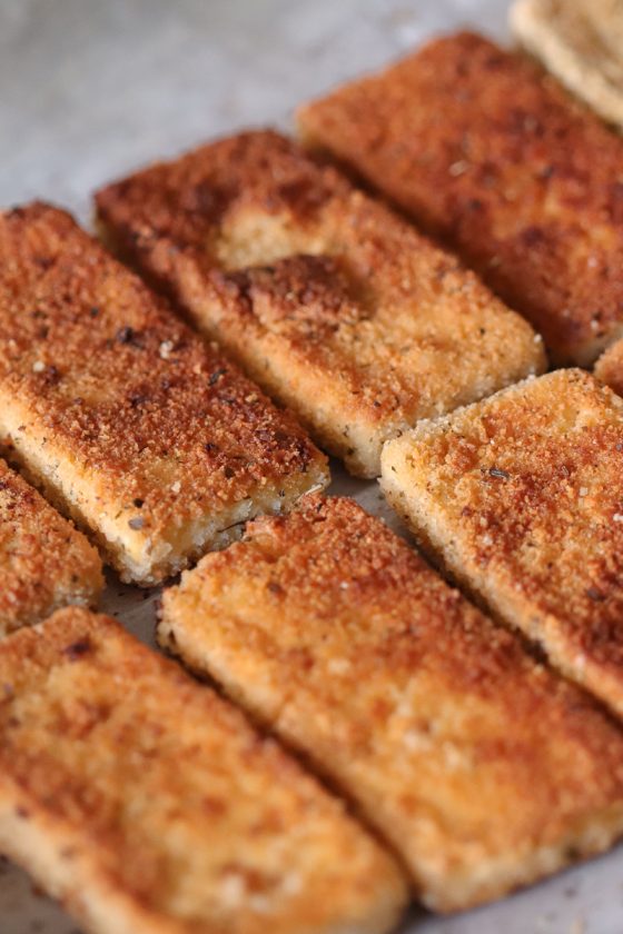 Crispy breaded and pan-fried vegan tofu cutlets lined up in a row. The breadcrumb coating looks golden brown and delicious.