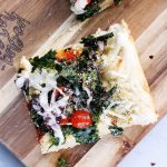 Vegan Crispy Kale Grandma-Style Pizza by Pasta-based. A top-down shot of a square slice of pizza on a cutting board.