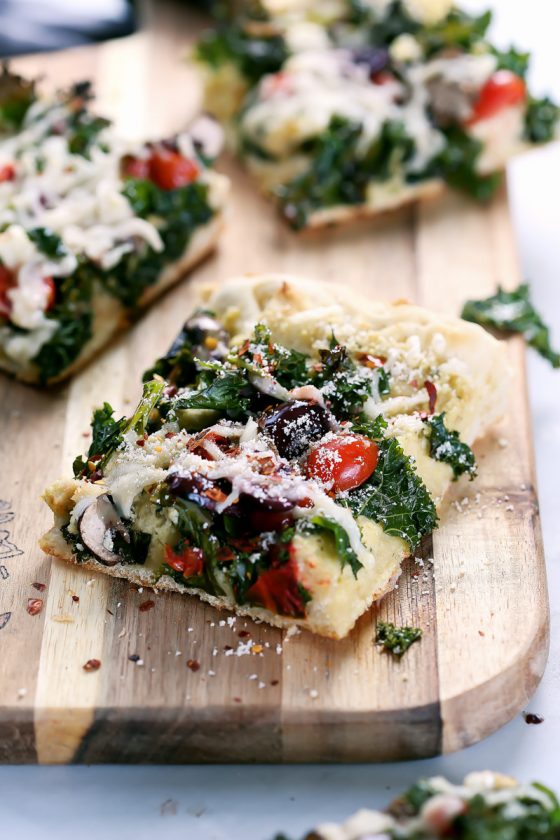 Vegan Crispy Kale Grandma-Style Pizza by Pasta-based. A square slice of pizza on a cutting board.