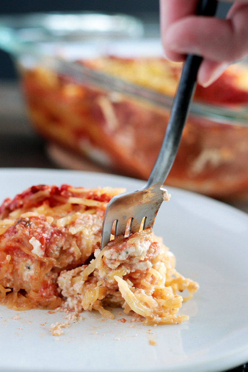 Spaghetti Squash Lasagna (Vegan and Gluten-free) by Pasta-based. Someone is taking a forkful of spaghetti squash lasagna with creamy vegan ricotta cheese melting out.