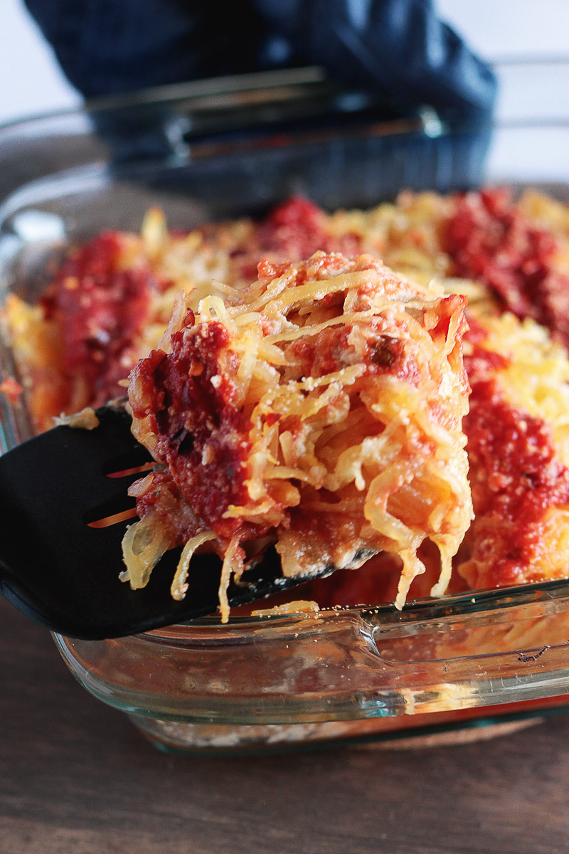 Spaghetti Squash Lasagna (Vegan and Gluten-free) by Pasta-based. A spatula reaches into the photo, taking a big scoop of vegan spaghetti squash lasagna out of a glass baking dish.