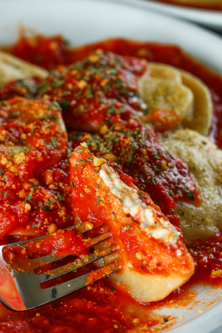 A ravioli in sauce cut in half, showing vegan ricotta cheese stuffing inside.