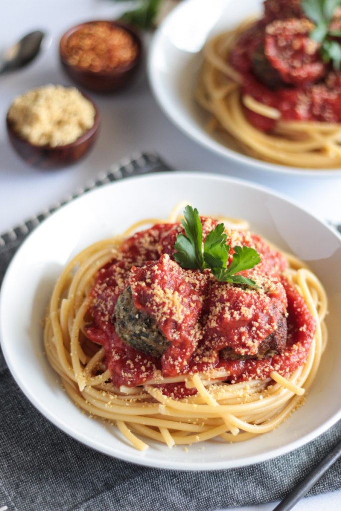 White plate with spaghetti and vegan meatballs covered in red sauce and parsley garnished.