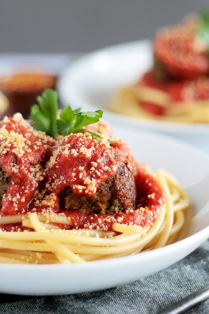 Crispy and browned vegan lentil meatballs on a bowl of spaghetti. Marinara sauce and vegan parmesan cheese on top.