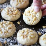 Vegan Italian Pignoli Cookies by Pasta-based. Someone is picking up a cookie from the tray.