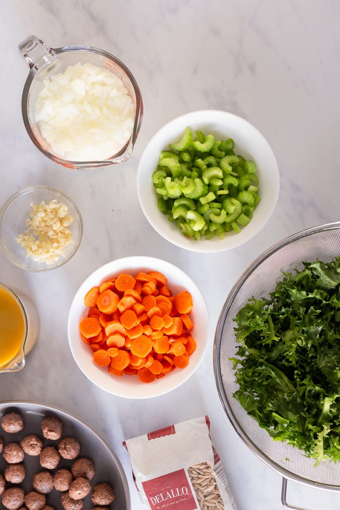 overhead photo of all ingredients for this vegan italian wedding soup recipe. Chopped onion, celery, garlic, carrots, escarole, uncooked meatballs, veggie broth and uncooked orzo pasta.