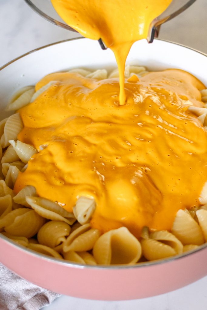 vegan mac and cheese sauce being poured from a blender into a big pan of pasta