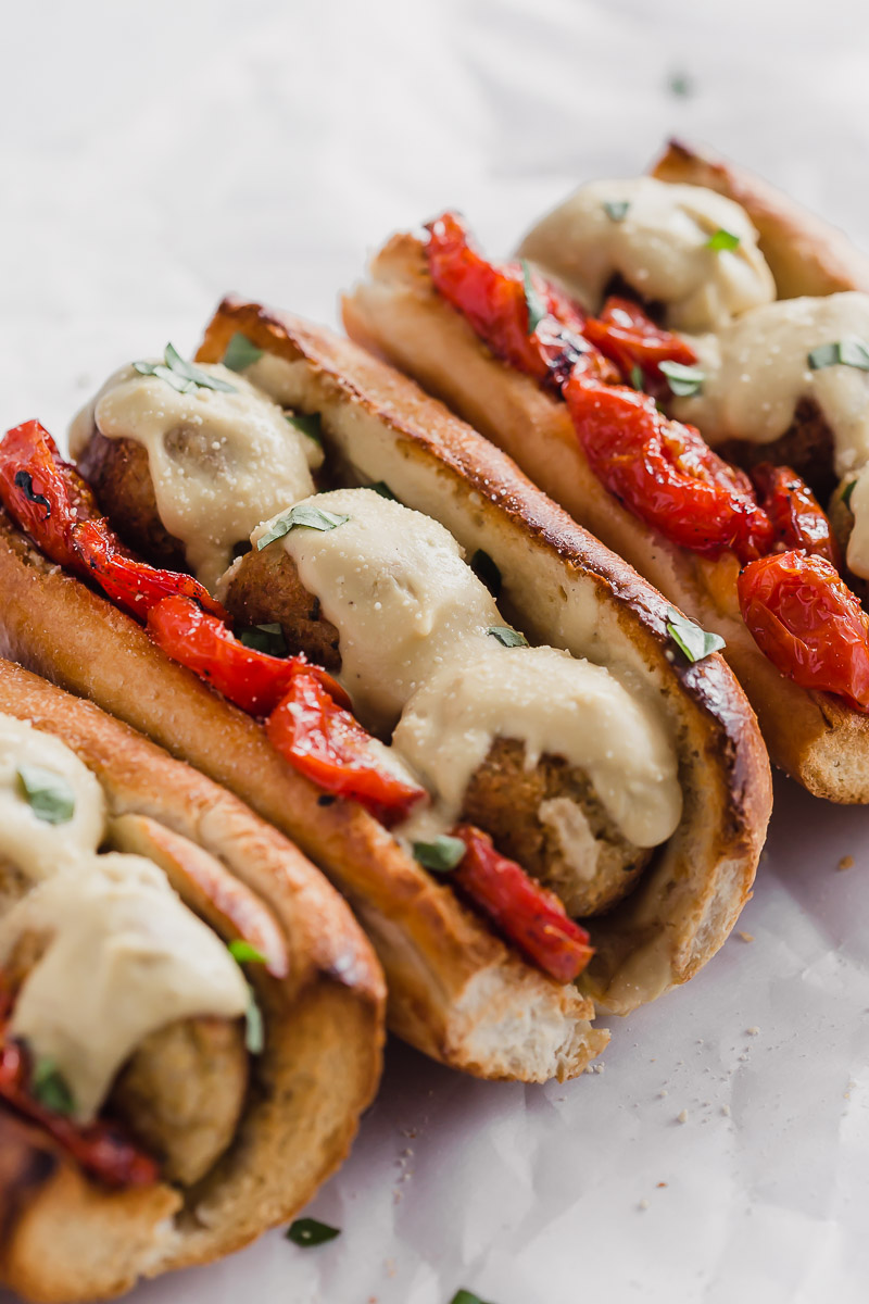 Vegan Meatball Subs by Pasta-based. Four meatball heroes on toasted garlic bread with roasted campari tomatoes, vegan cauliflower alfredo sauce, and cauliflower brown rice meatballs with fresh basil sprinkled around.