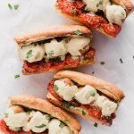 Vegan Meatball Subs by Pasta-based. Four meatball heroes on toasted bread with roasted campari tomatoes, vegan cauliflower alfredo sauce, and cauliflower brown rice meatballs with fresh basil sprinkled around.