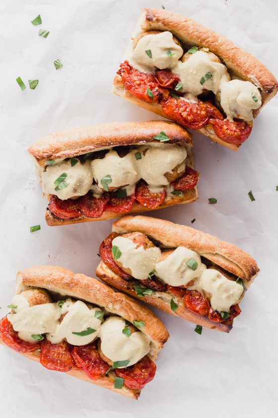 Vegan Meatball Subs by Pasta-based. Four meatball heroes on toasted bread with roasted campari tomatoes, vegan cauliflower alfredo sauce, and cauliflower brown rice meatballs with fresh basil sprinkled around.