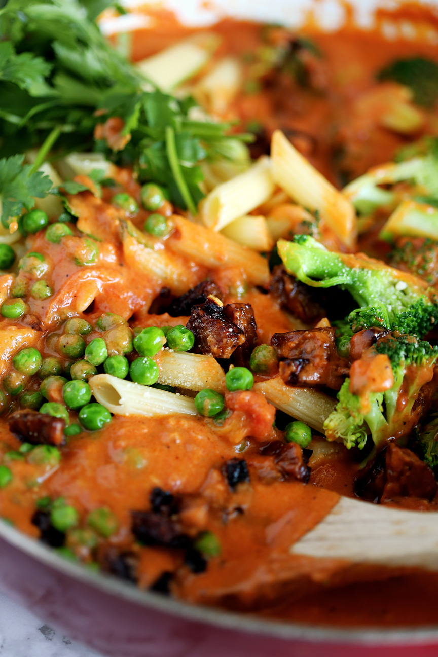 Red sauce in a pan with penne pasta, peas, broccoli, tempeh pancetta and parsley.