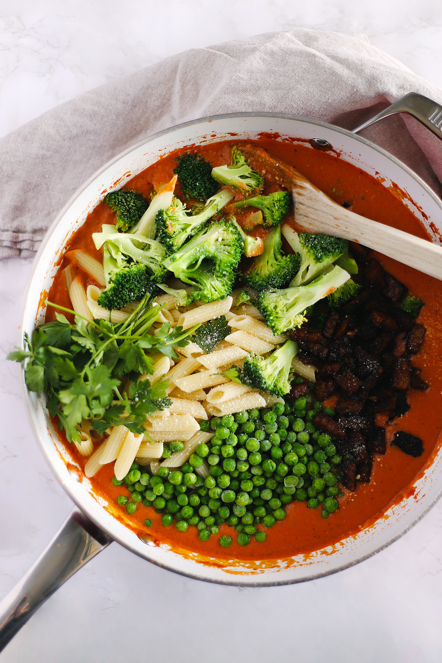 Redsauce in a pan with penne pasta, peas, broccoli, tempeh pancetta and parsley.