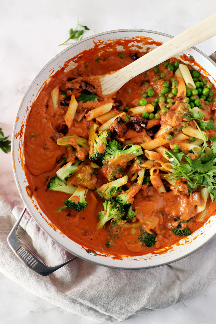 Red sauce in a pan with penne pasta, peas, broccoli, tempeh pancetta and parsley.