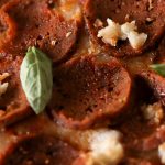 Close up picture of vegan pepperoni on a pizza with tiny green basil leaves scattered.