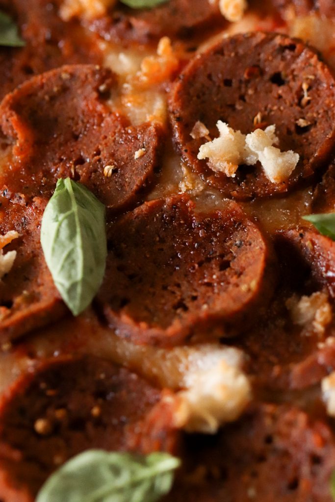 Close up picture of vegan pepperoni on a pizza with tiny green basil leaves scattered.