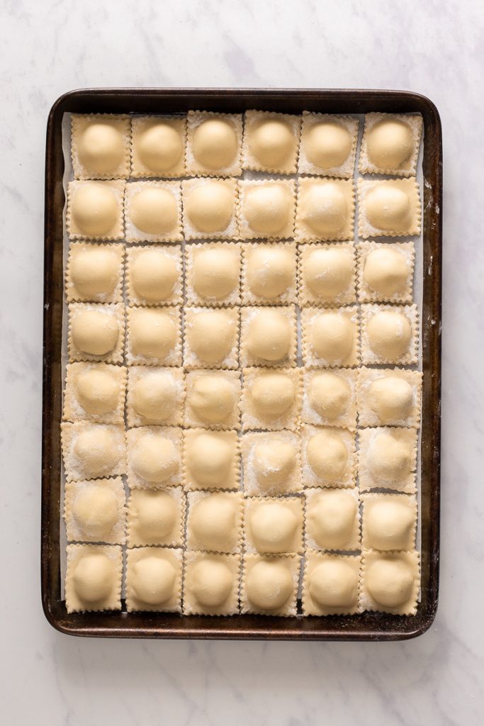 A baking sheet full of 48 uniform raviolis.