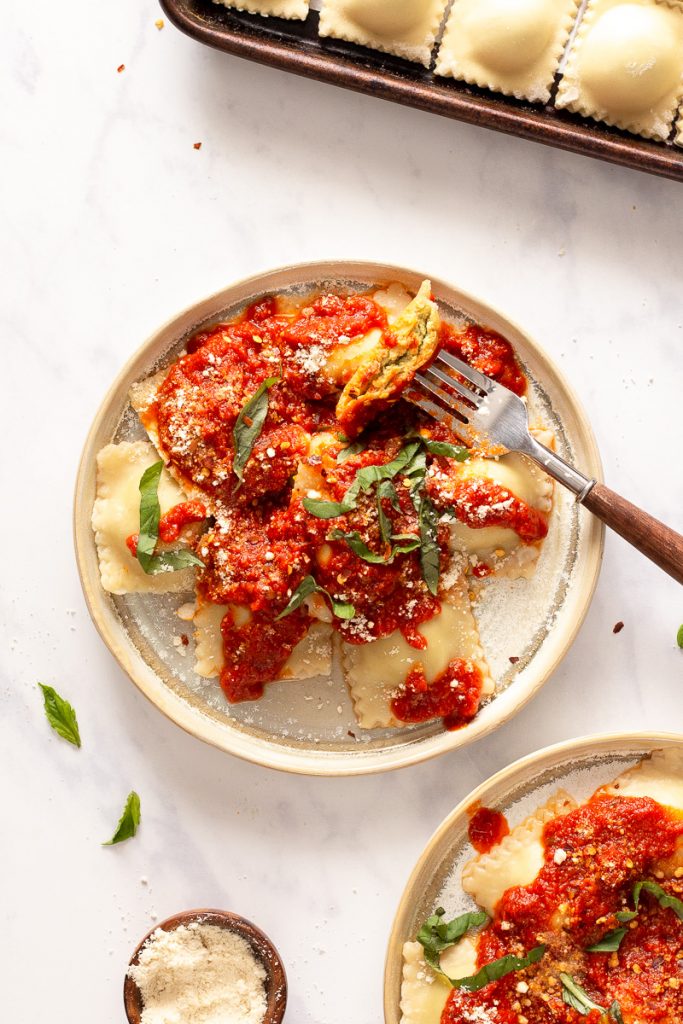 Overhead photo of a plate of vegan ravioli with red sauce on top garnished with basil.