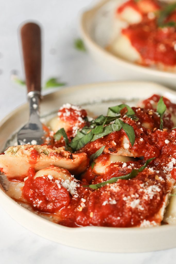 Photo of a plate of vegan ravioli with red sauce on top garnished with basil.  One ravioli is cut in half held by a fork.