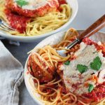 Vegan Seitan Parmesan by Pasta-based. Bowls of spaghetti with seitan cutlets smothered in marinara sauce and topped with vegan mozzarella cheese. A fork with a piece of seitan leaning on the side of the bowl.