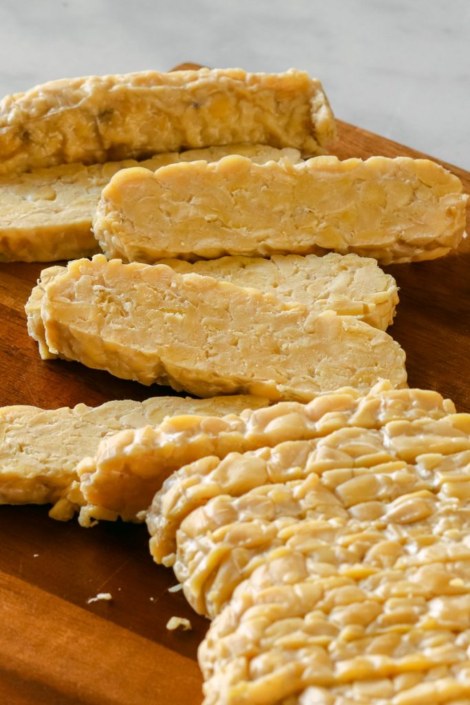 raw tempeh close up cut into strips on a dark brown cutting board.