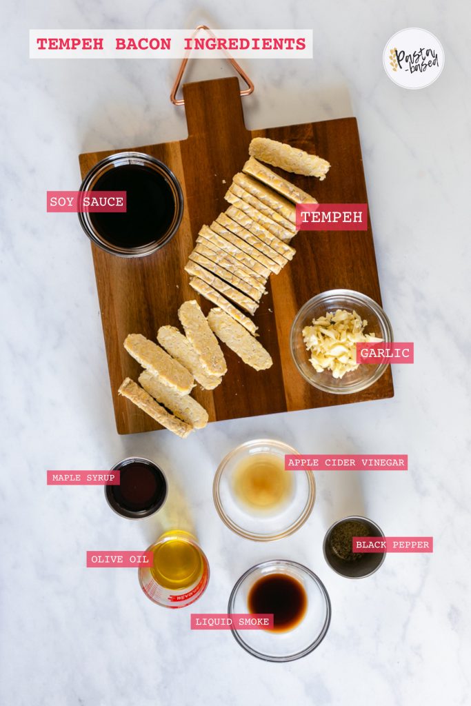 overhead graphic showing all ingredients to make this recipe.  Sliced tempeh on a brown cutting board, soy sauce, minced garlic, maple syrup, apple cider vinegar, olive oil, black pepper and liquid smoke.