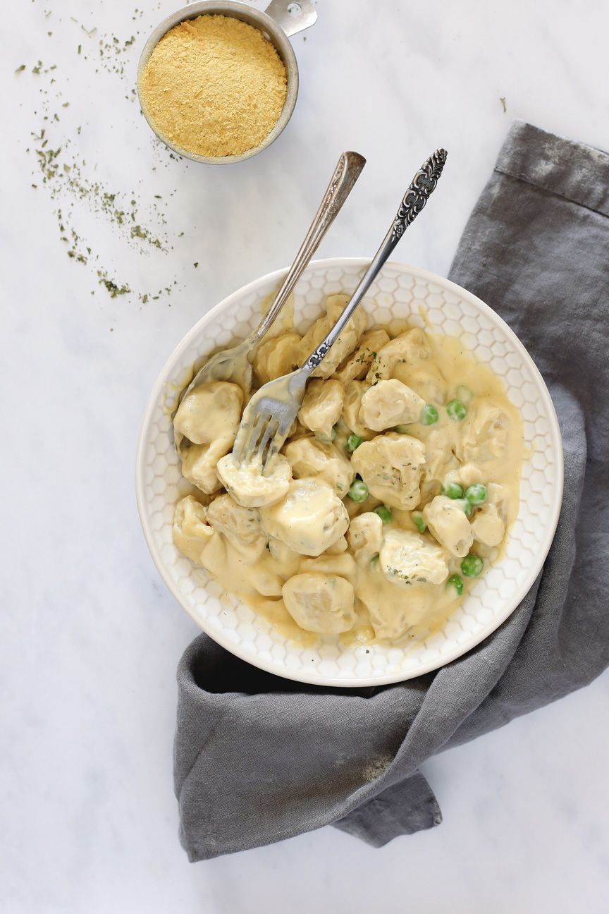 A bowl of vegan tortellini mixed with creamy alfredo sauce and peas on top of a grey linen towel.