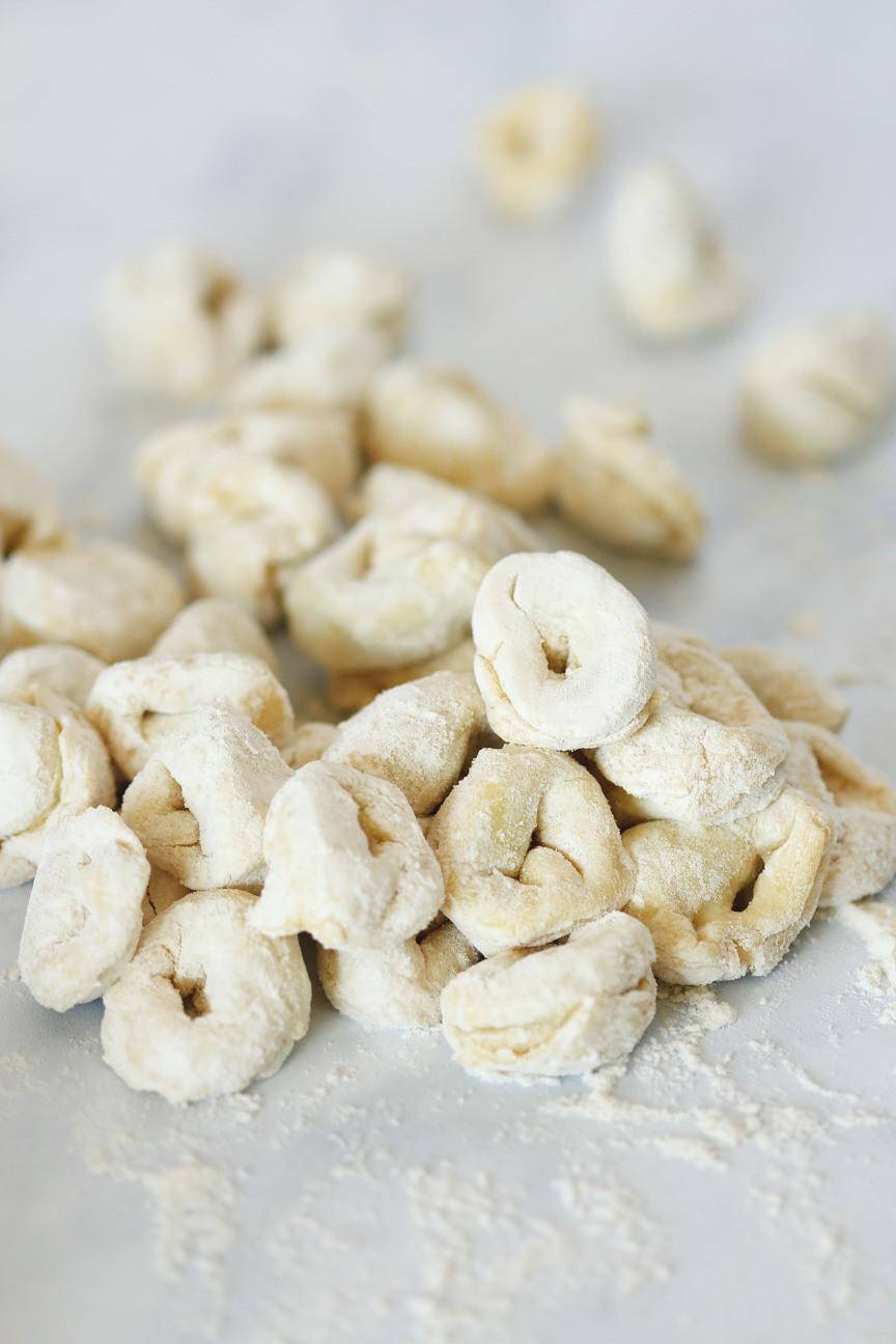 Raw vegan tortellini, just rolled and piled up on a white countertop. Flour sprinkled around them to prevent sticking.