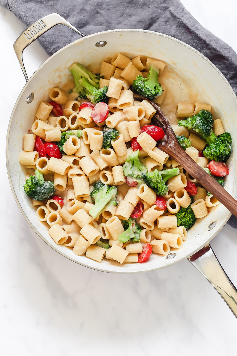 Vegan White Bean Alfredo by Pasta-based. Creamy, cheesy, healthy, low-calorie and low-fat vegan alfredo sauce made with white beans, garlic, and vegetable broth. A large pan filled with mezze rigatoni pasta, smothered in creamy white bean alfredo sauce and tossed with fresh broccoli and grape tomatoes.